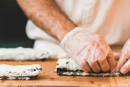 Gloved hands making sushi roll.