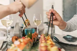 Hands with chopsticks grabbing sushi.